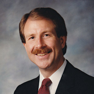 Bill Montgomery smiles in front of a light background in 1990.