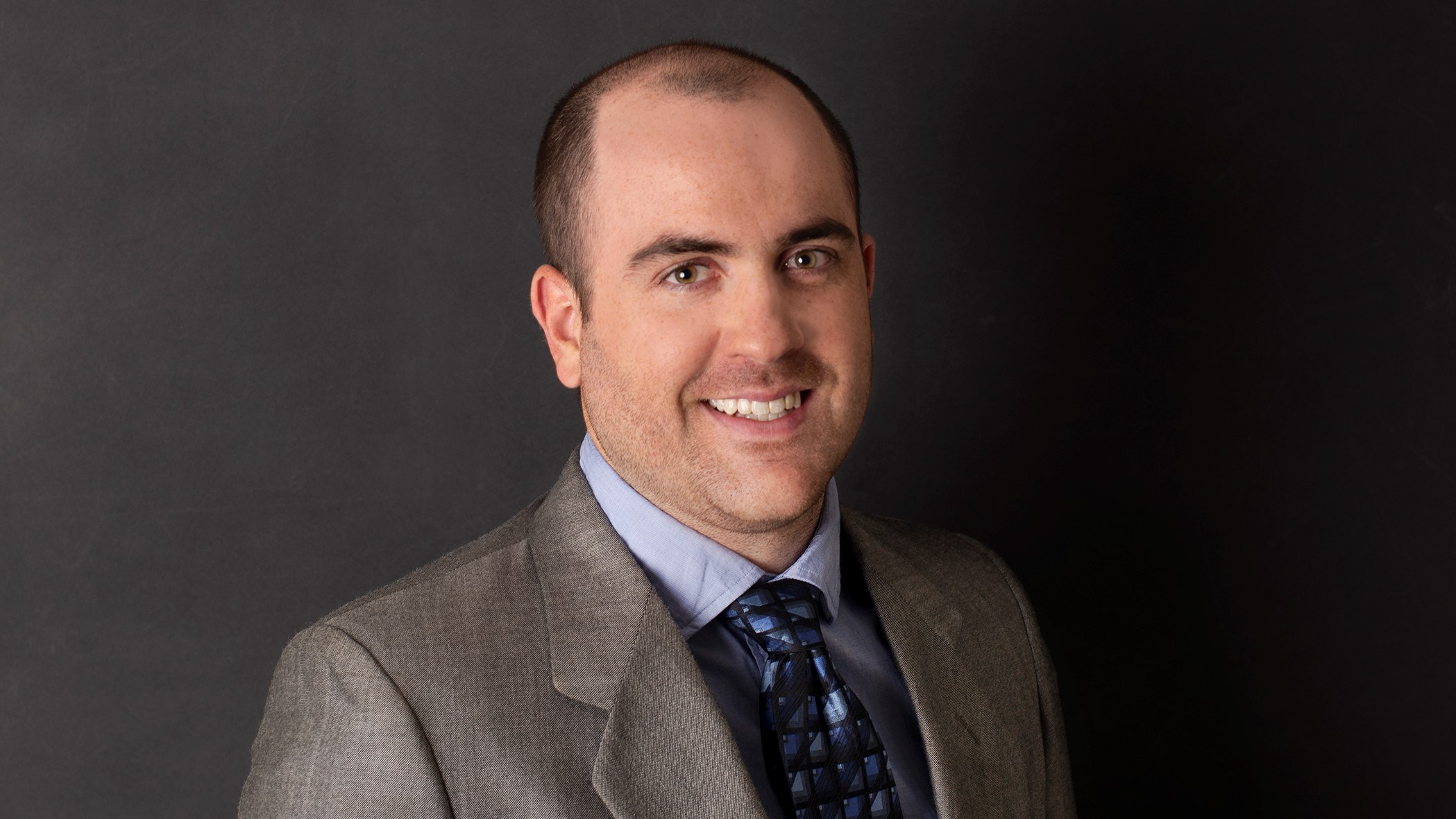 Scott Miller, Associate Marketing Representative, smiles in front of a black background.