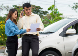 A middle-aged couple looking at some paperwork in front of a car