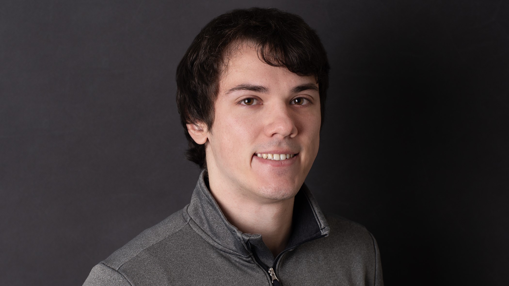 Zachary Lyons, Quality Assurance Analyst II at Celina Insurance Group, smiles in front of a black background.