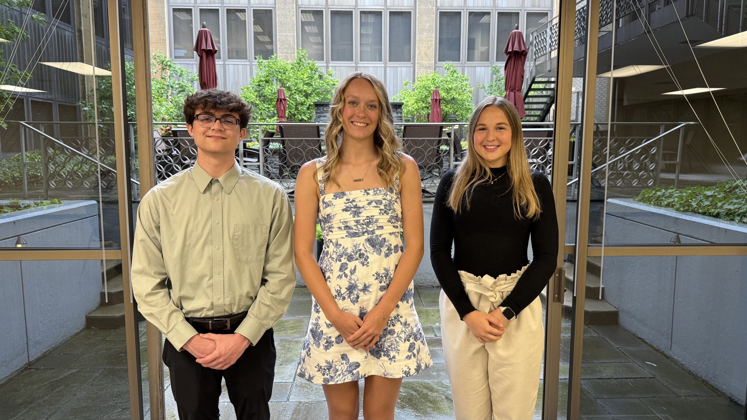 High school scholarship winners Gavin Fisher, Brynn Egbert and Olivia Broering stand in front of an open door looking out over a garden courtyard.