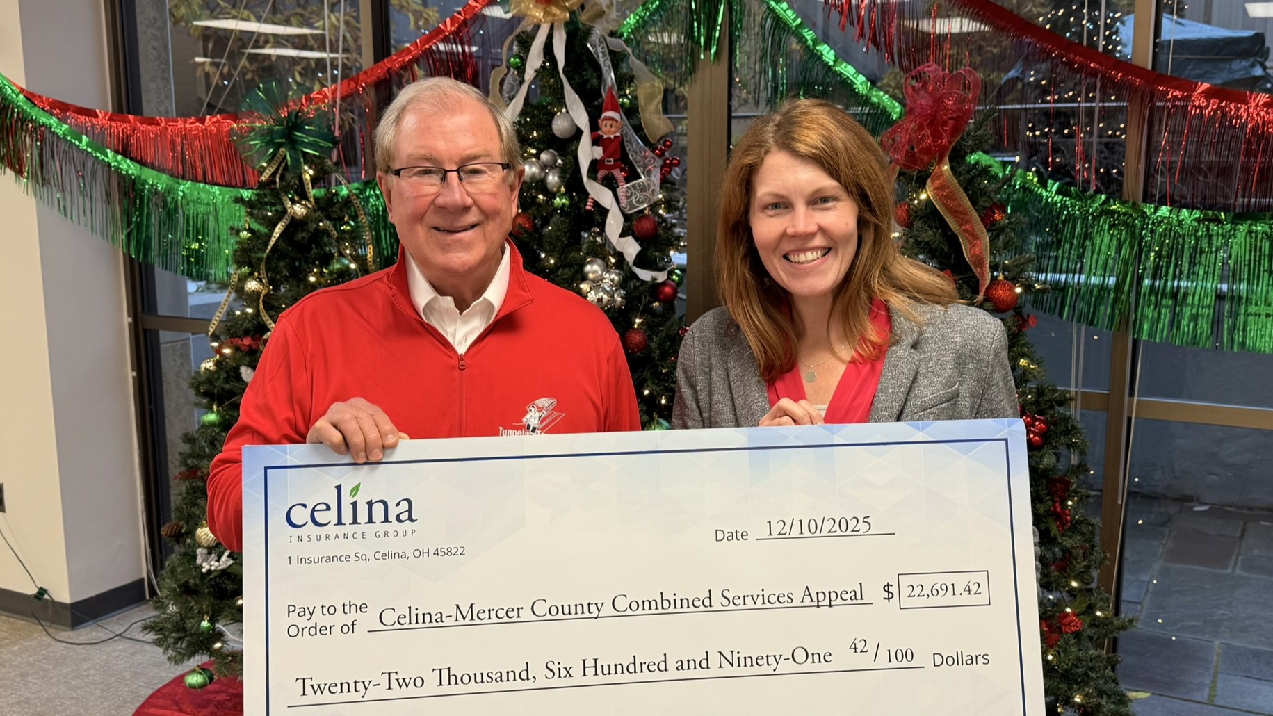 Celina President and CEO Bill Montgomery presents a check to Celina-Mercer County Combined Services Appeal Vice President Caitlin Bair in front of decorated Christmas trees.