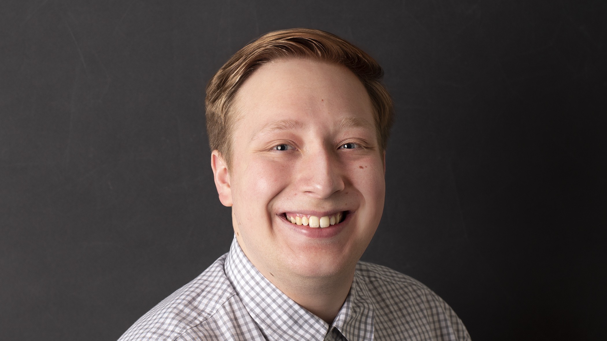 Connor Glass, Associate Actuary at Celina Insurance Group, smiles in front of a black background